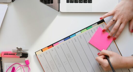 person holding pencil and stick note beside table